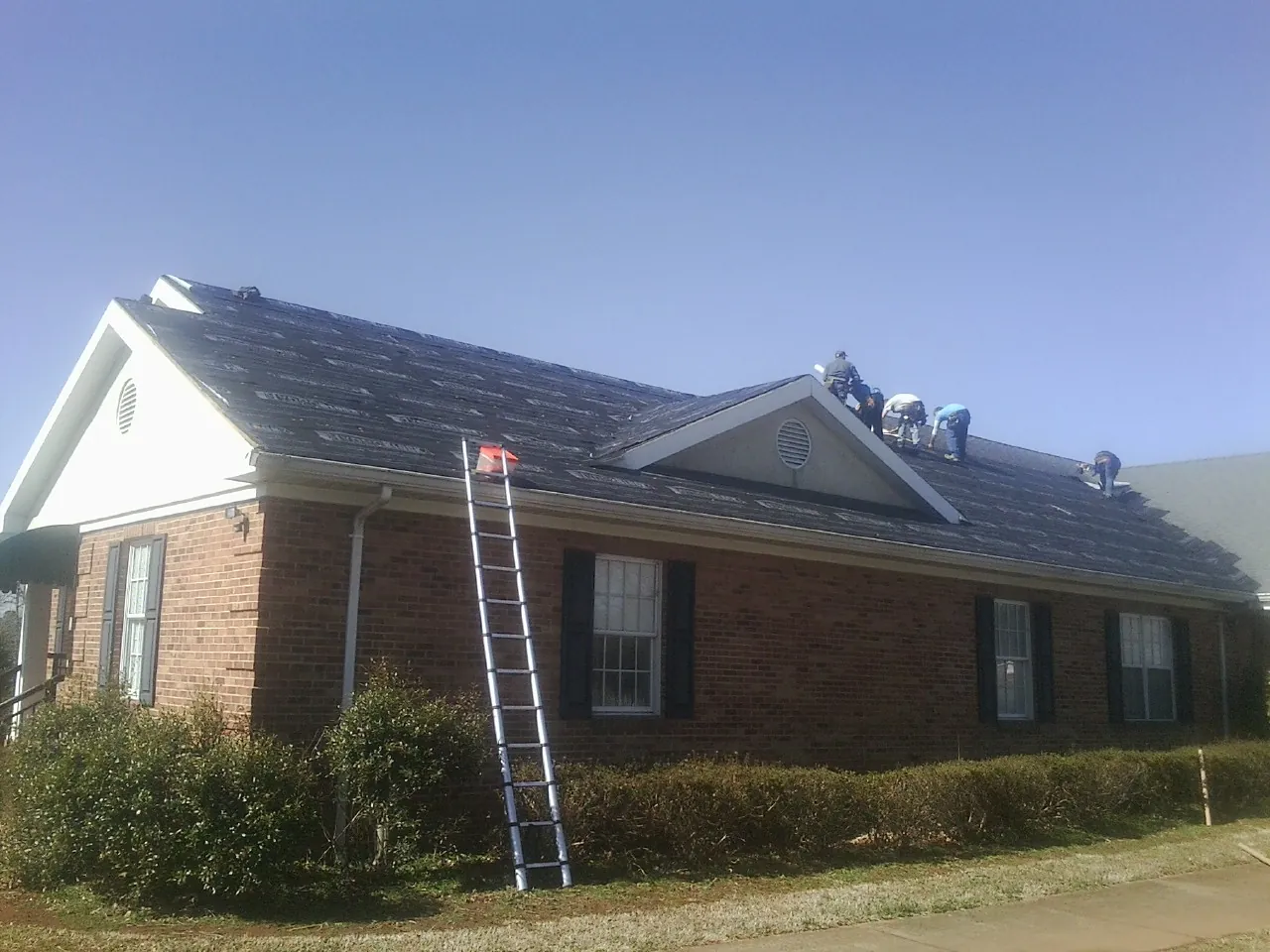 Crew tearing shingles off a brick ranch roof with a ladder set — Metal Roof Repair work by our crew in Torrington