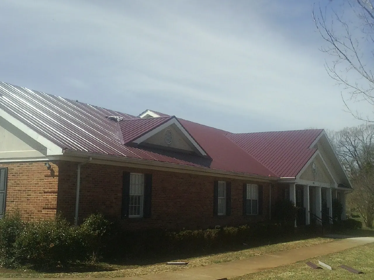Red metal roof with gabled entries on a long brick building, from a Hail Damage Roof Repair job in Torrington