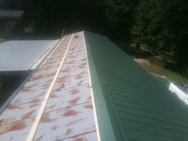 Old rusted panels beside newly installed green metal roofing in Torrington