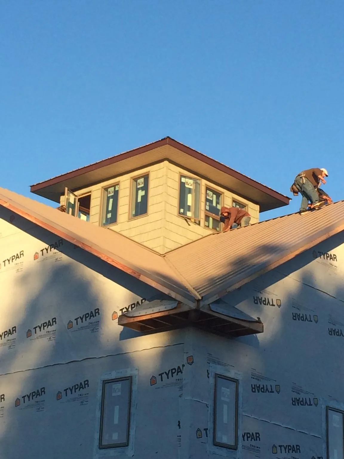 Roofers working around a rooftop cupola on a new metal roof at sunset — Roof Waterproofing in Torrington by Roofing Brothers